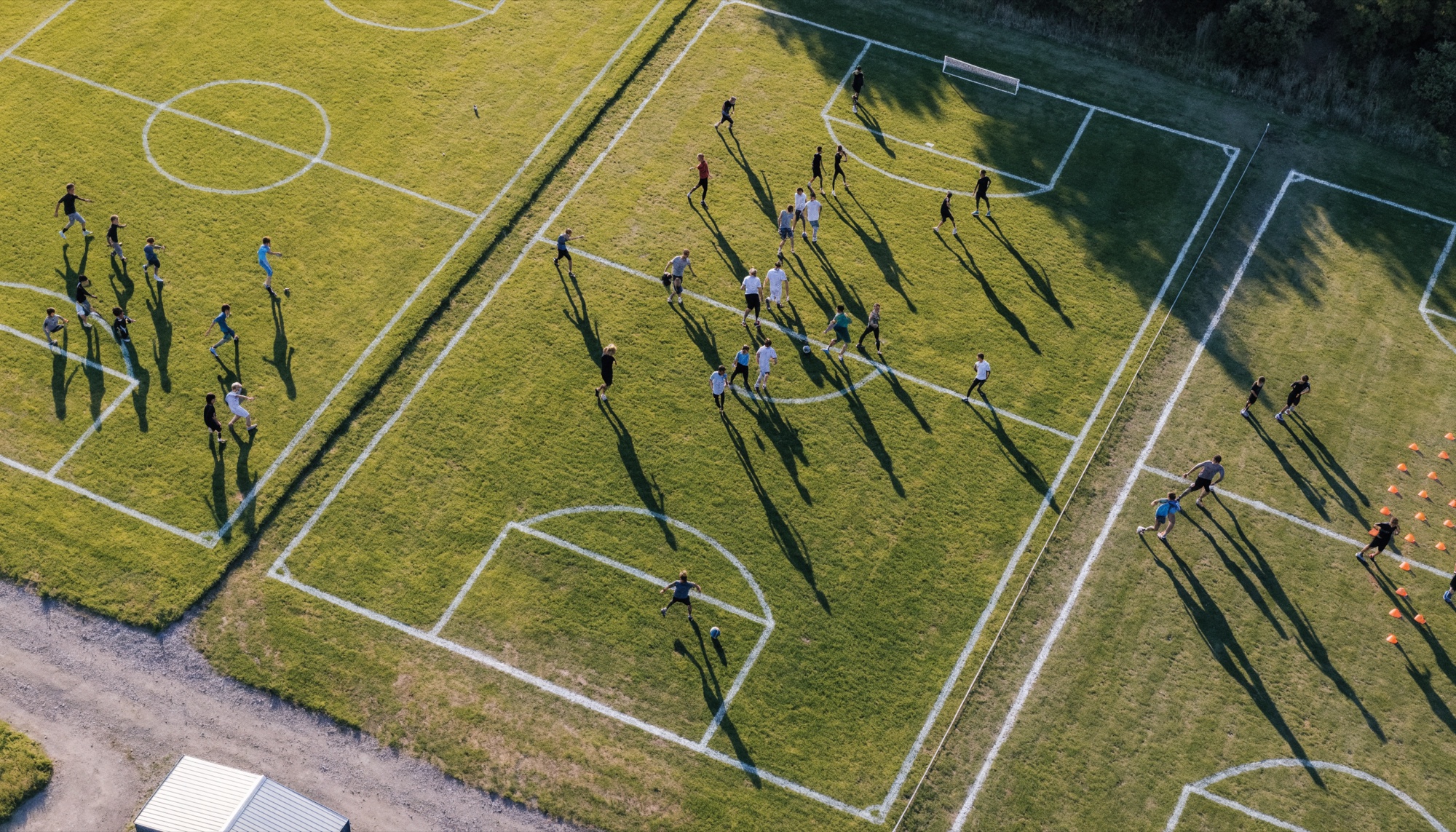 Aerial view of grassroots pitches on a Saturday morning — a kids' match, an adult game and a training drill in progress